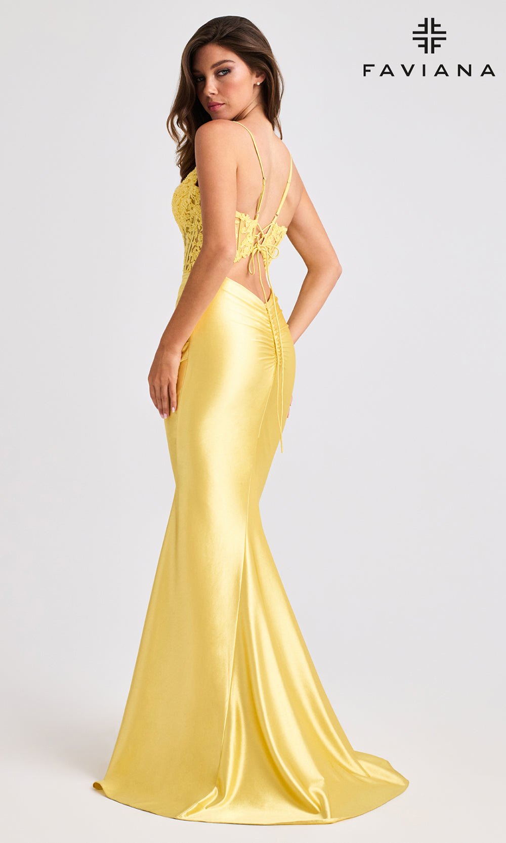 Woman wearing a yellow evening gown with lace detailing, standing against a white background. FAVIANA brand visible.