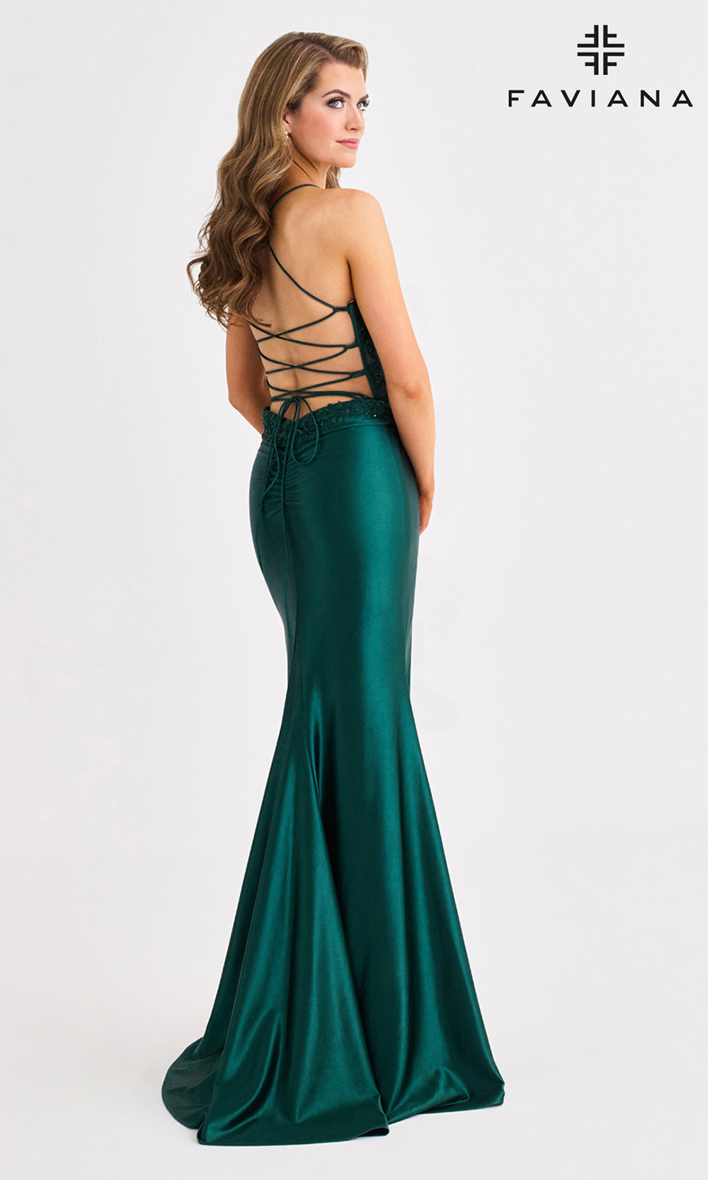Woman wearing a green evening gown with lace-up back, branded 'Faviana'.