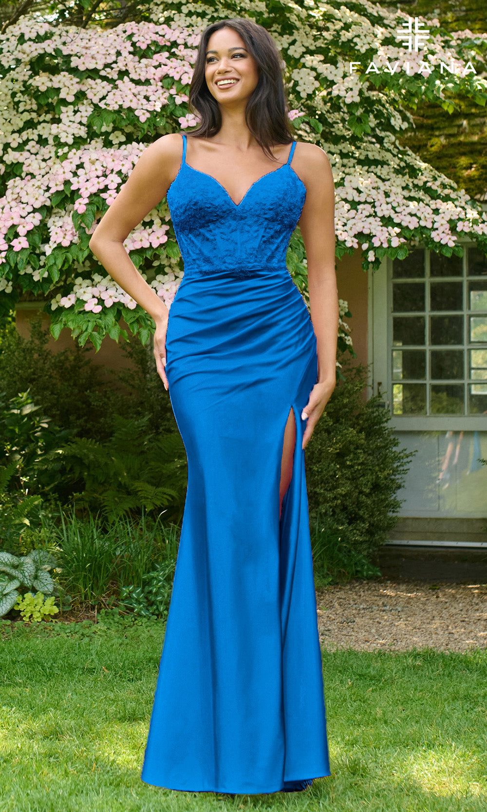 Woman in a blue evening gown standing outdoors with greenery and flowers in the background