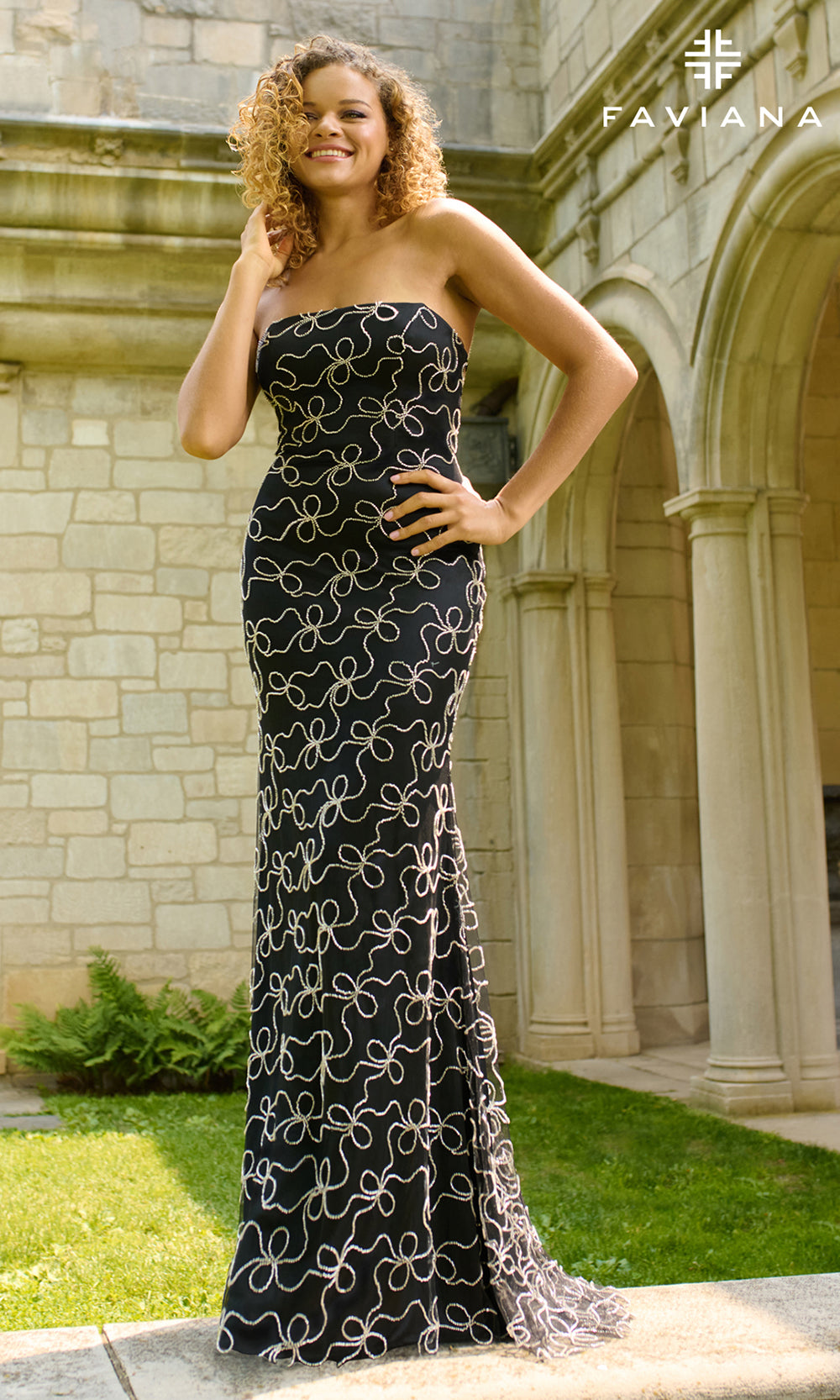 Woman in a strapless black evening gown with white patterns standing in front of a stone building.