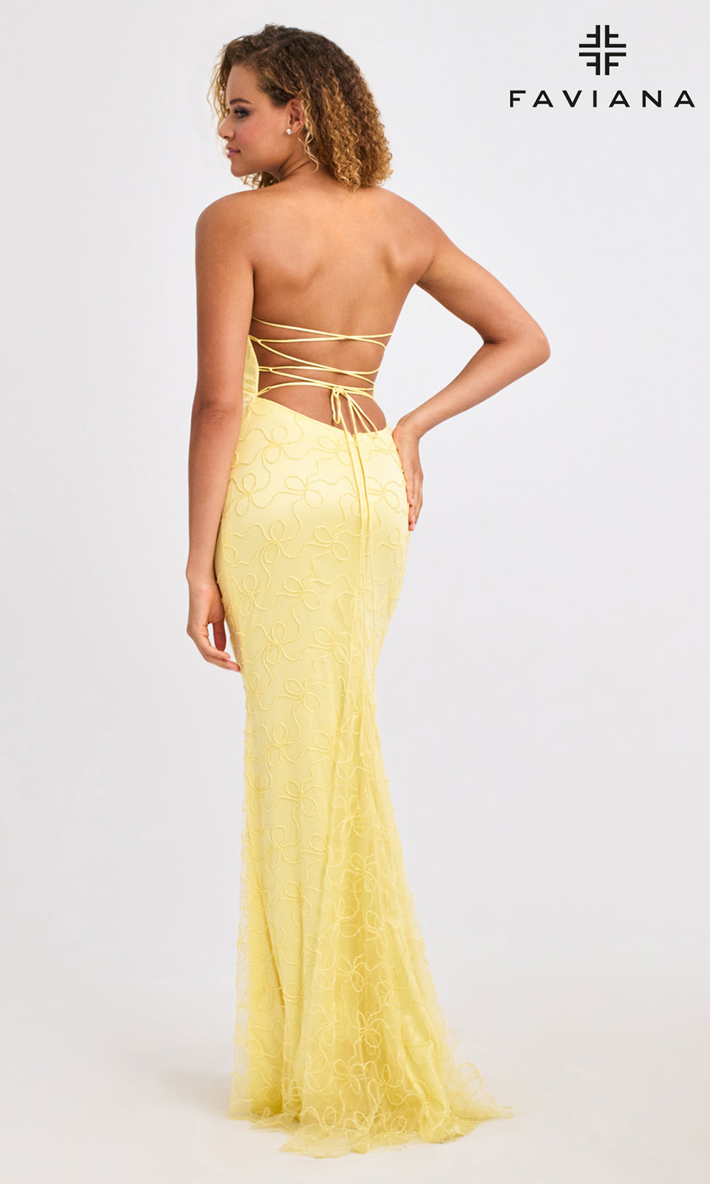 Woman wearing a yellow evening gown with lace-up back, branded 'Faviana'.