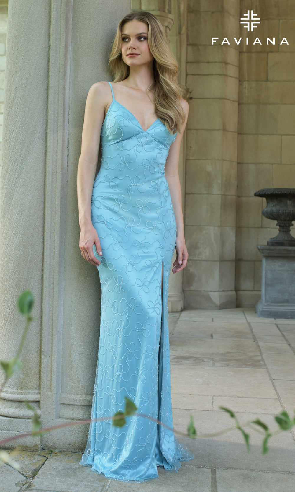 Woman wearing a light blue evening gown with a slit, standing outdoors.