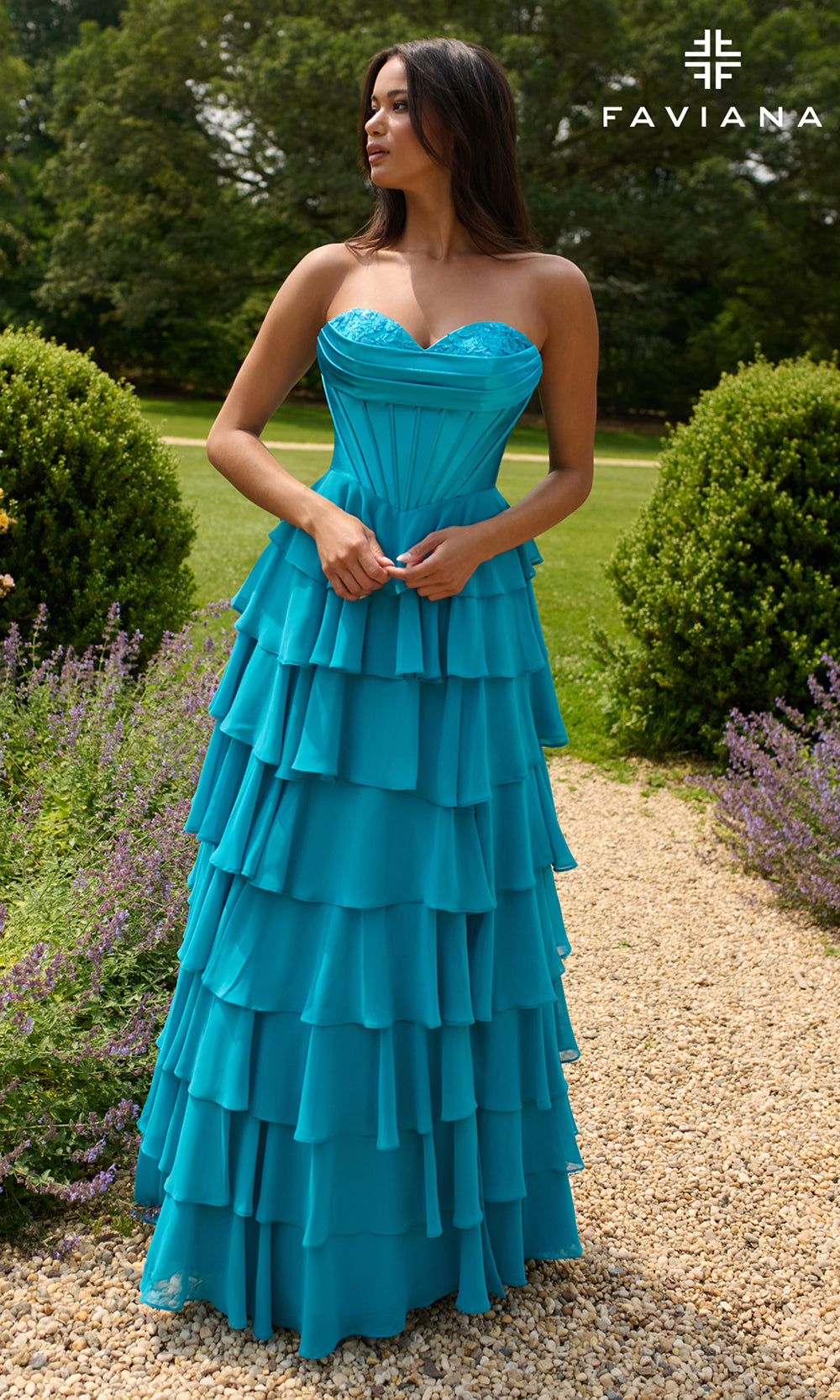 Woman wearing a blue strapless gown with ruffled layers in an outdoor setting, branded 'Faviana'.
