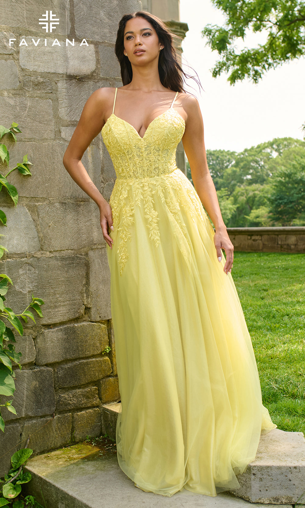 Woman in a yellow evening gown standing outdoors near a stone wall.