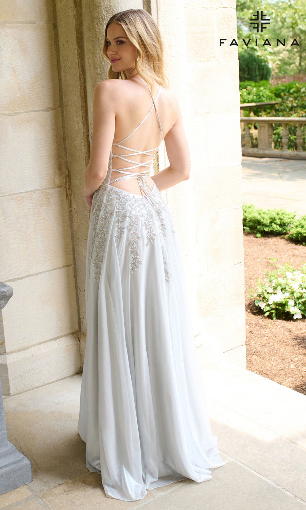 Woman in a silver evening gown with open back standing outdoors.