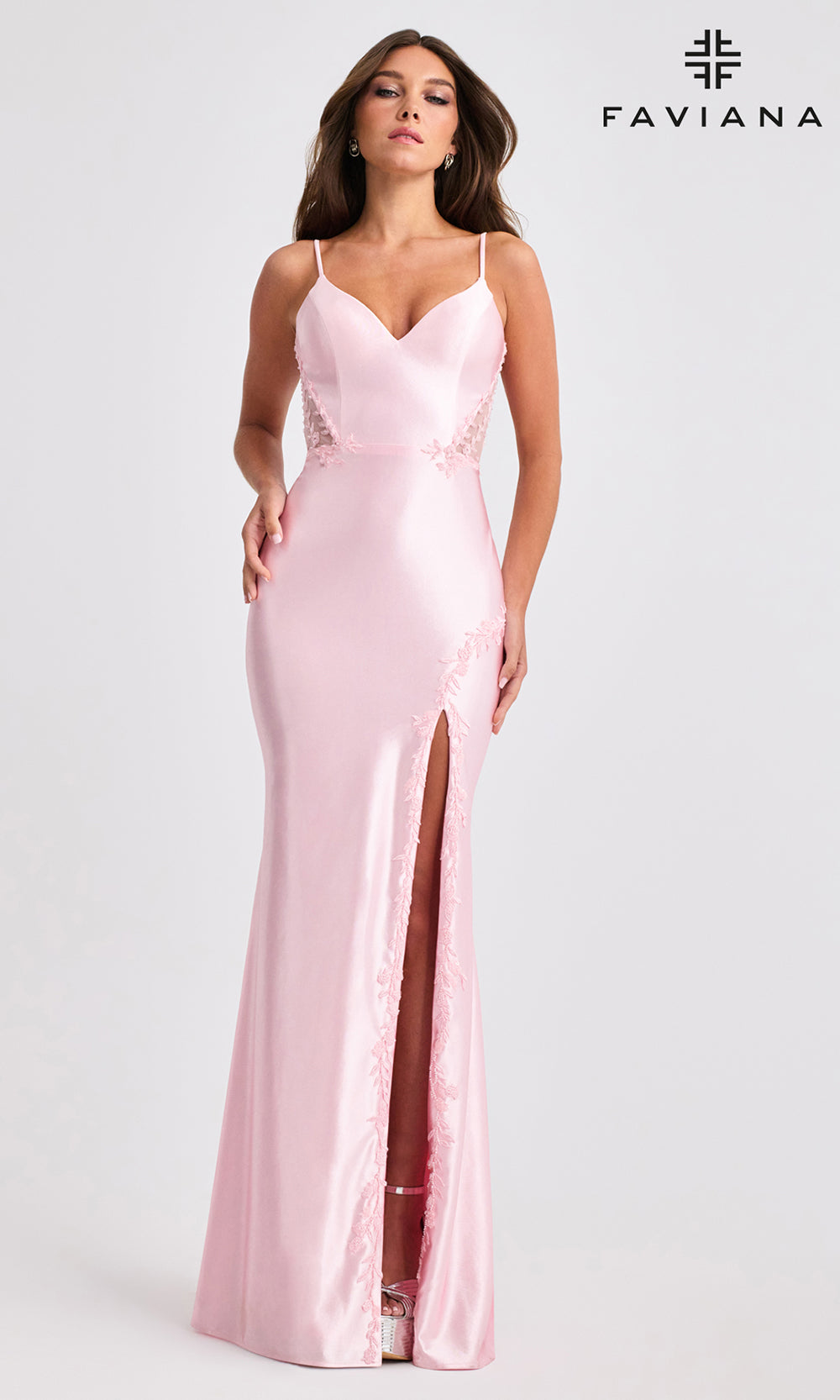 Woman wearing a pink satin evening gown with a slit on a white background, branded 'Faviana'.