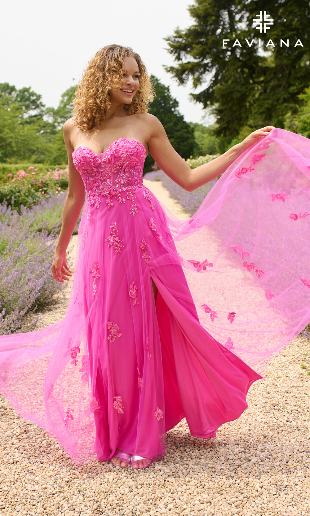 Woman in a pink evening gown with floral details standing outdoors.
