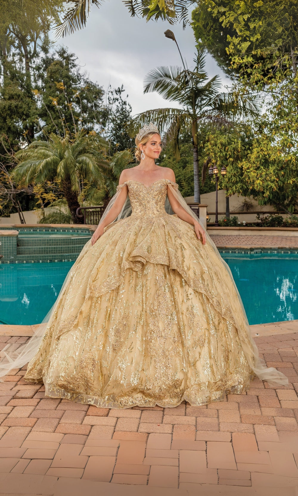 Woman in a gold ball gown standing by a pool with trees in the background