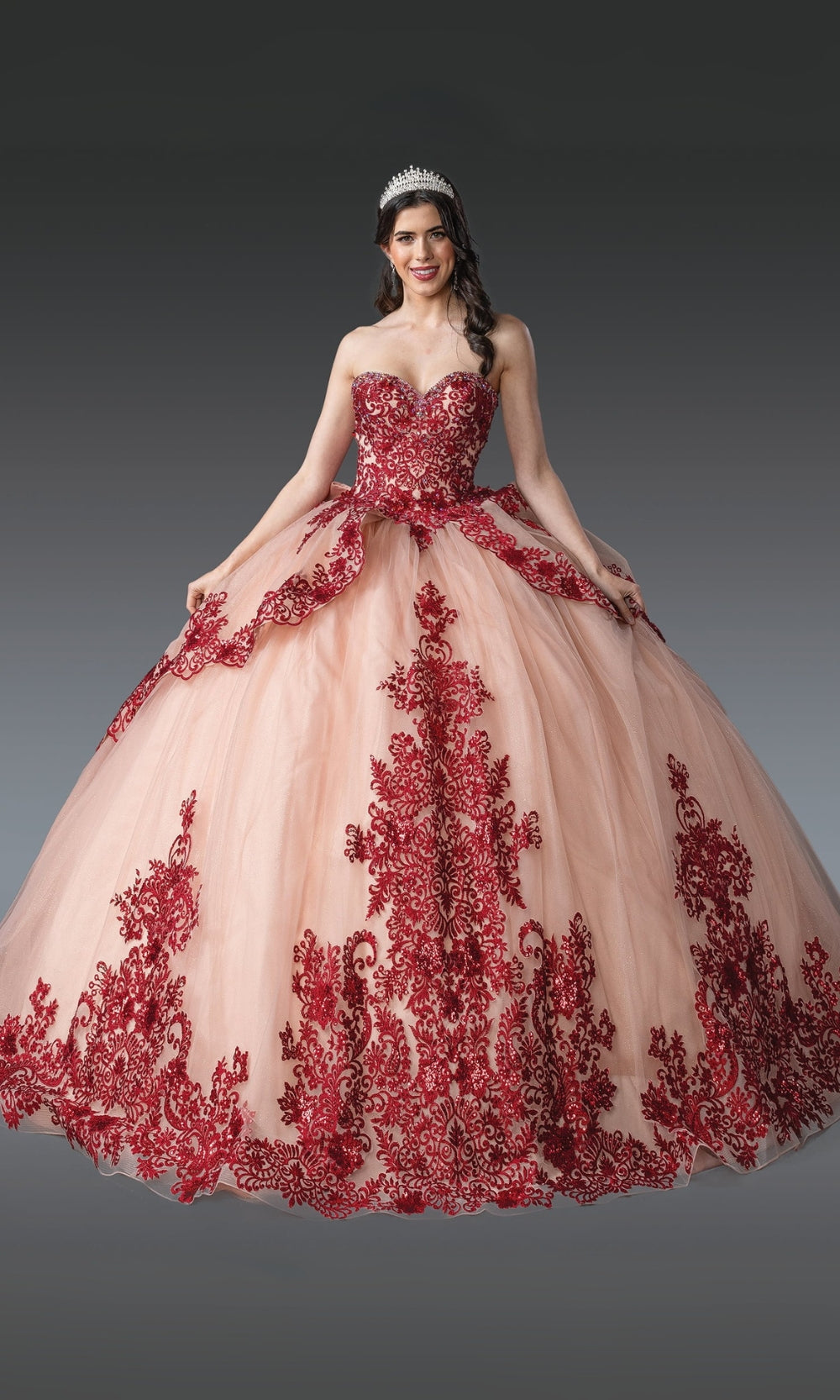 Woman wearing a pink and red ball gown with floral embroidery on a gray background