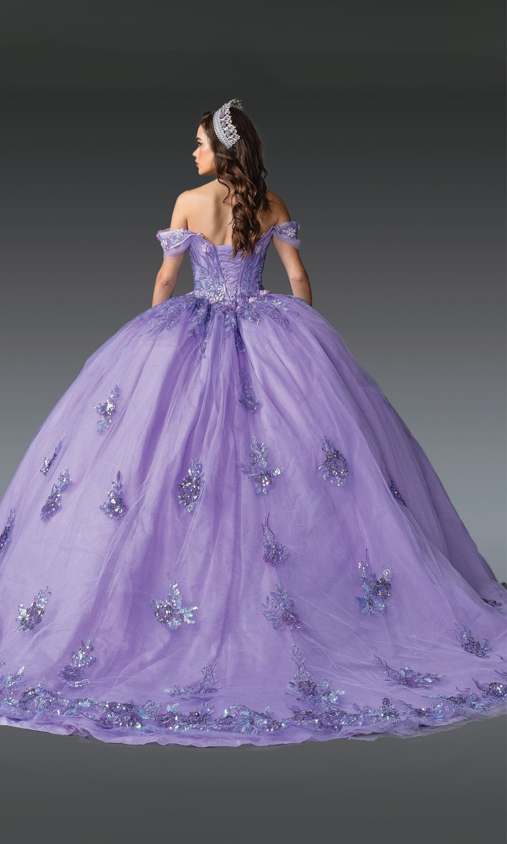 Woman wearing a purple quinceanera dress with floral embellishments on a gray background