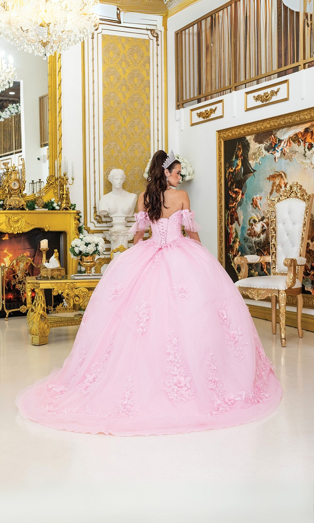Woman in a pink gown standing in an opulent room with gold decor and a fireplace.