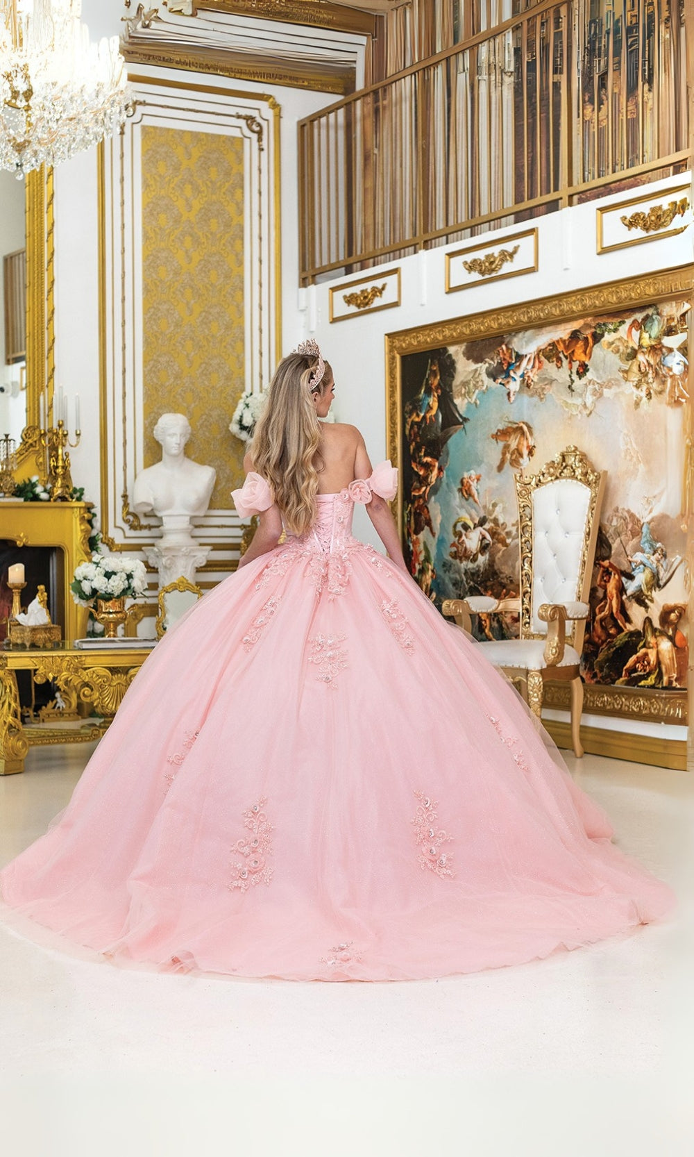 Woman in a pink gown standing in an ornate room with gold accents and classical art.