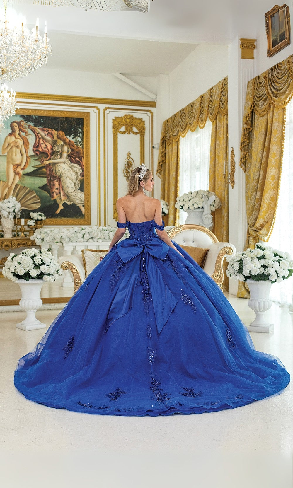 Woman in a blue gown standing in an ornate room with gold accents and classical art.