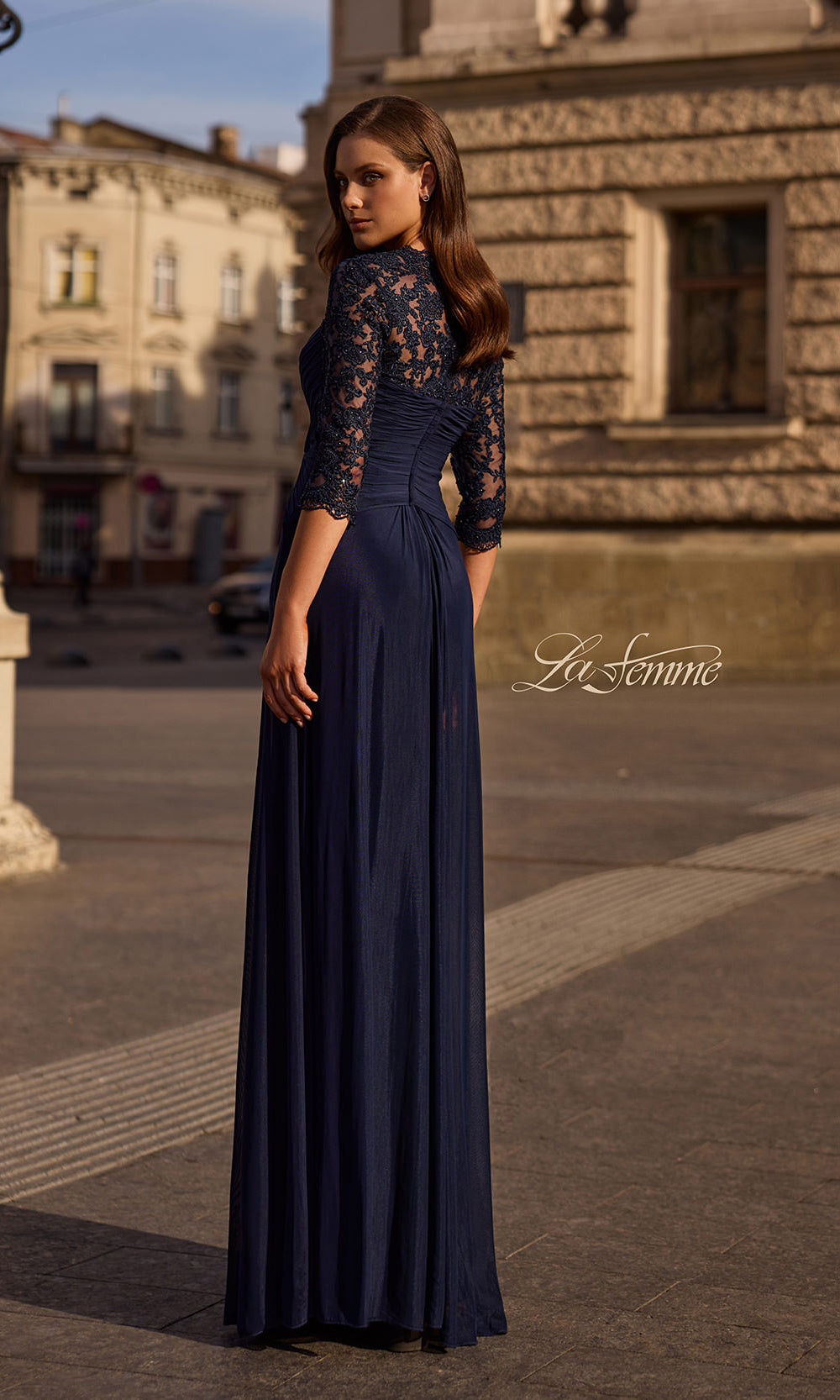 Woman in a long dark blue dress with floral sleeves standing on a street.