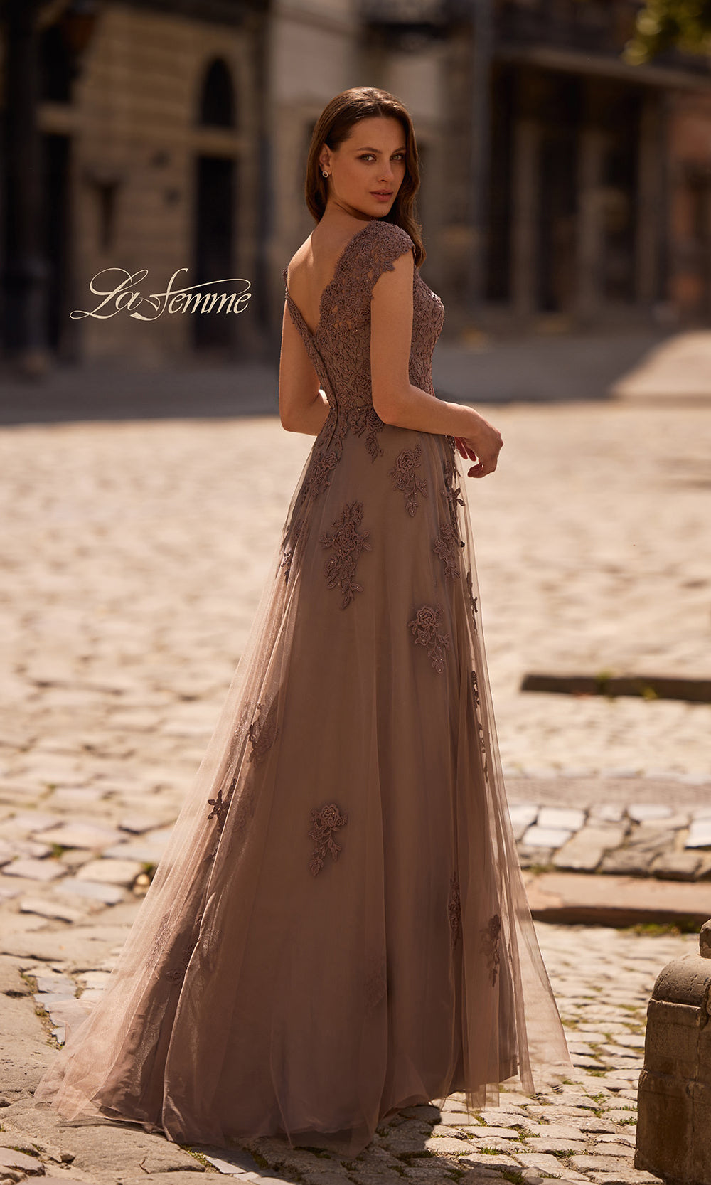 Woman in a elegant brown evening gown standing on a cobblestone street.