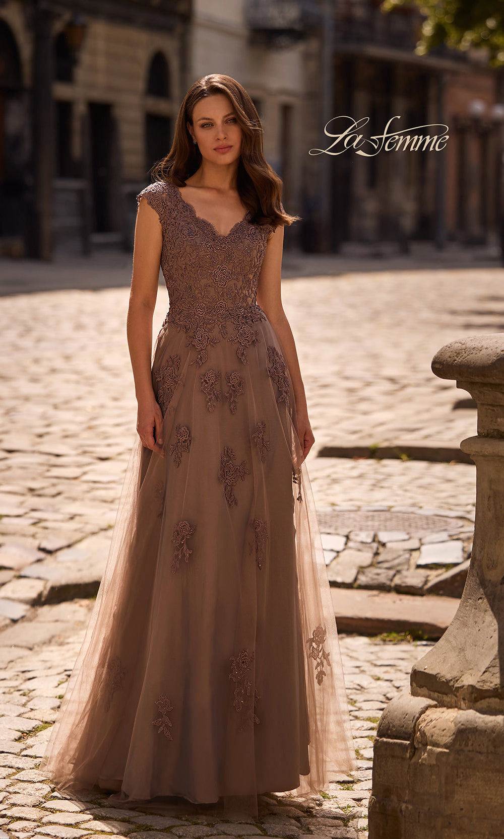 Woman in a long, elegant dress standing on a cobblestone street with 'La Femme' branding.