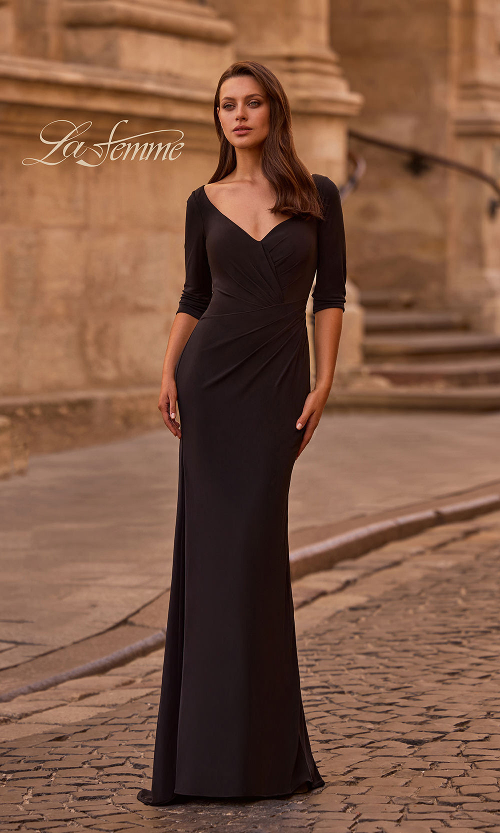 Woman in a black evening gown standing in front of a stone building with 'La Femme' branding.