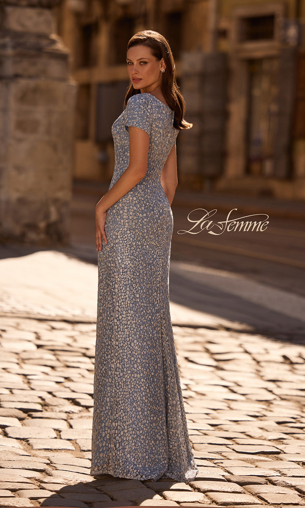 Woman in a long, patterned dress standing on a cobblestone street with 'La Femme' branding.