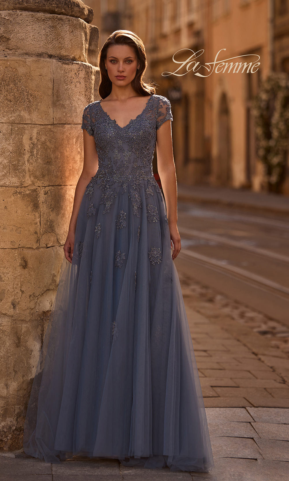 Woman in a long, elegant dress standing against a stone wall with 'La Femme' branding.