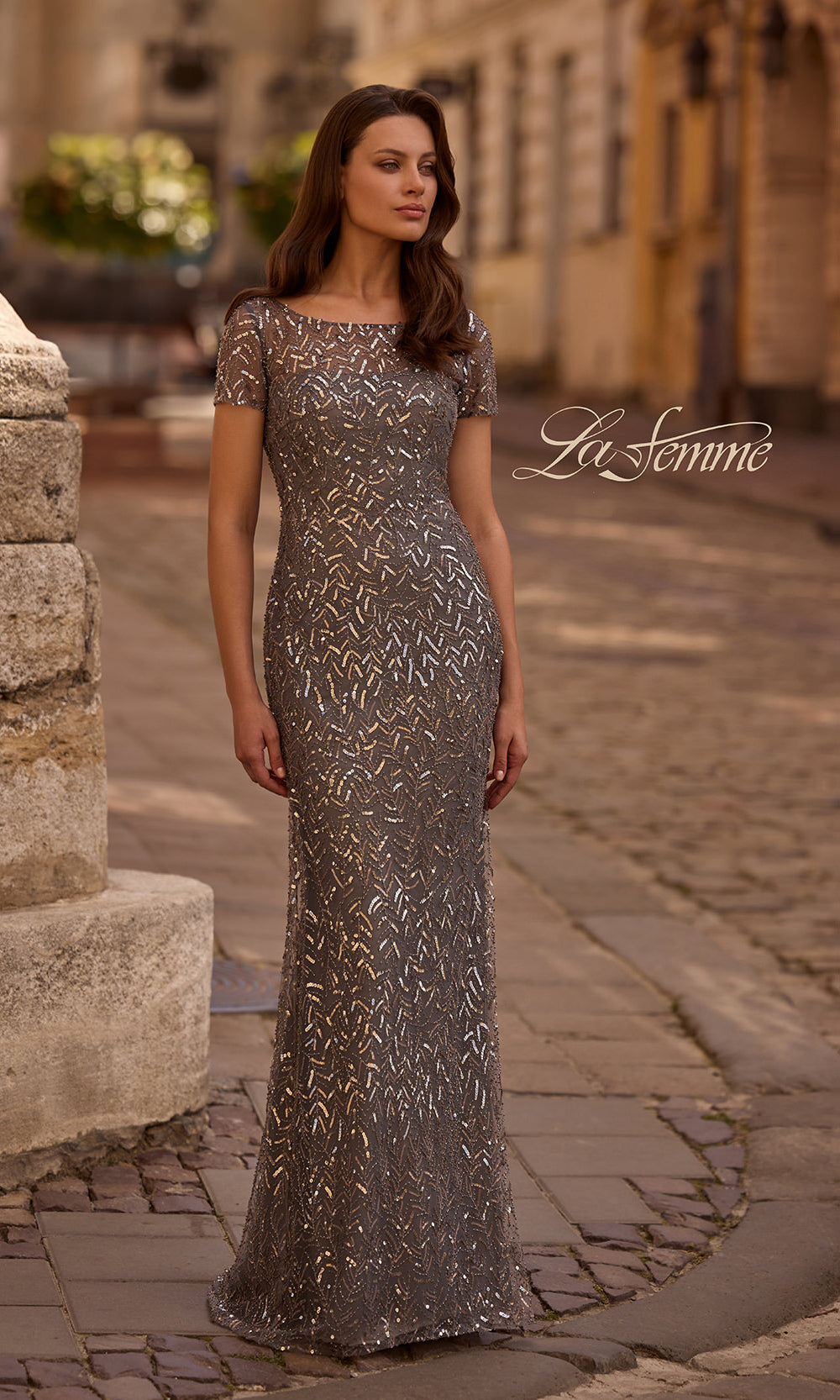 Woman wearing a silver evening gown on a cobblestone street with 'La Femme' branding.