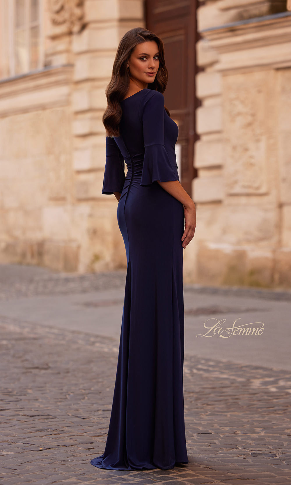 Woman in a navy blue evening gown standing in front of a stone building.