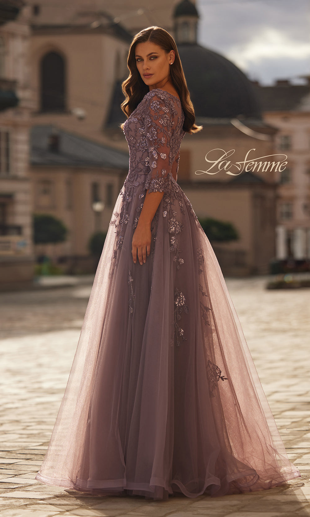 Woman in a pink evening gown standing in an outdoor setting with 'La Femme' branding.