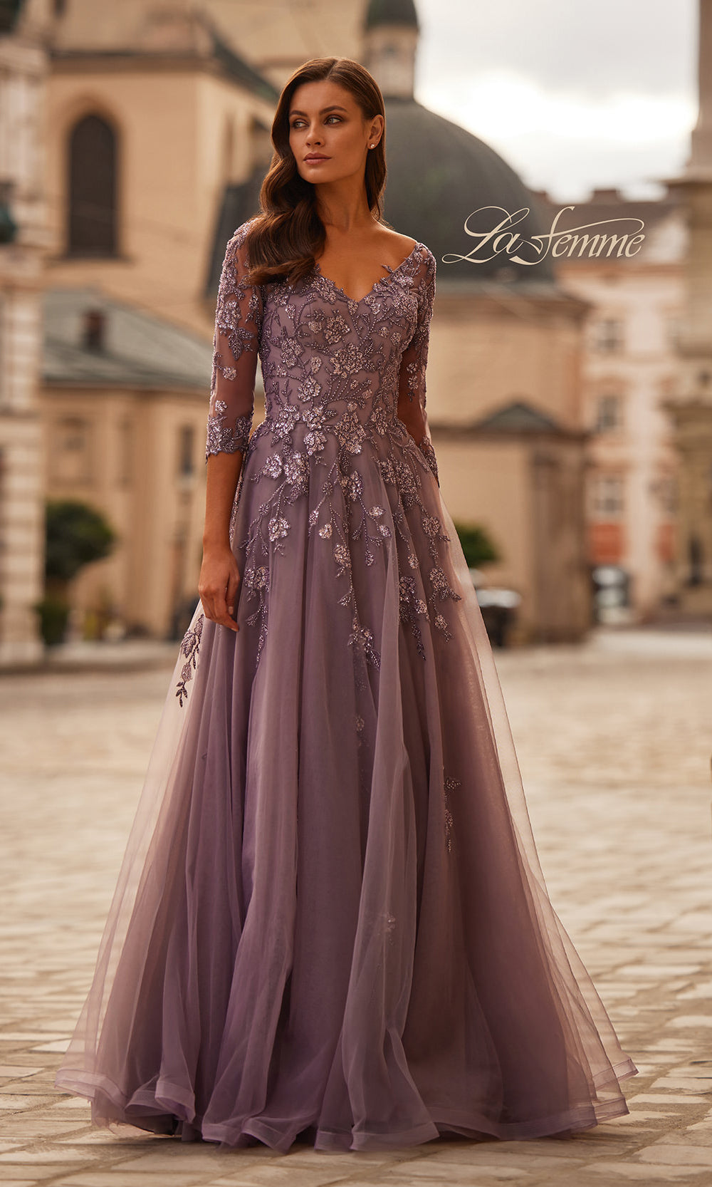 Woman wearing a purple evening gown with floral lace details in an outdoor setting.