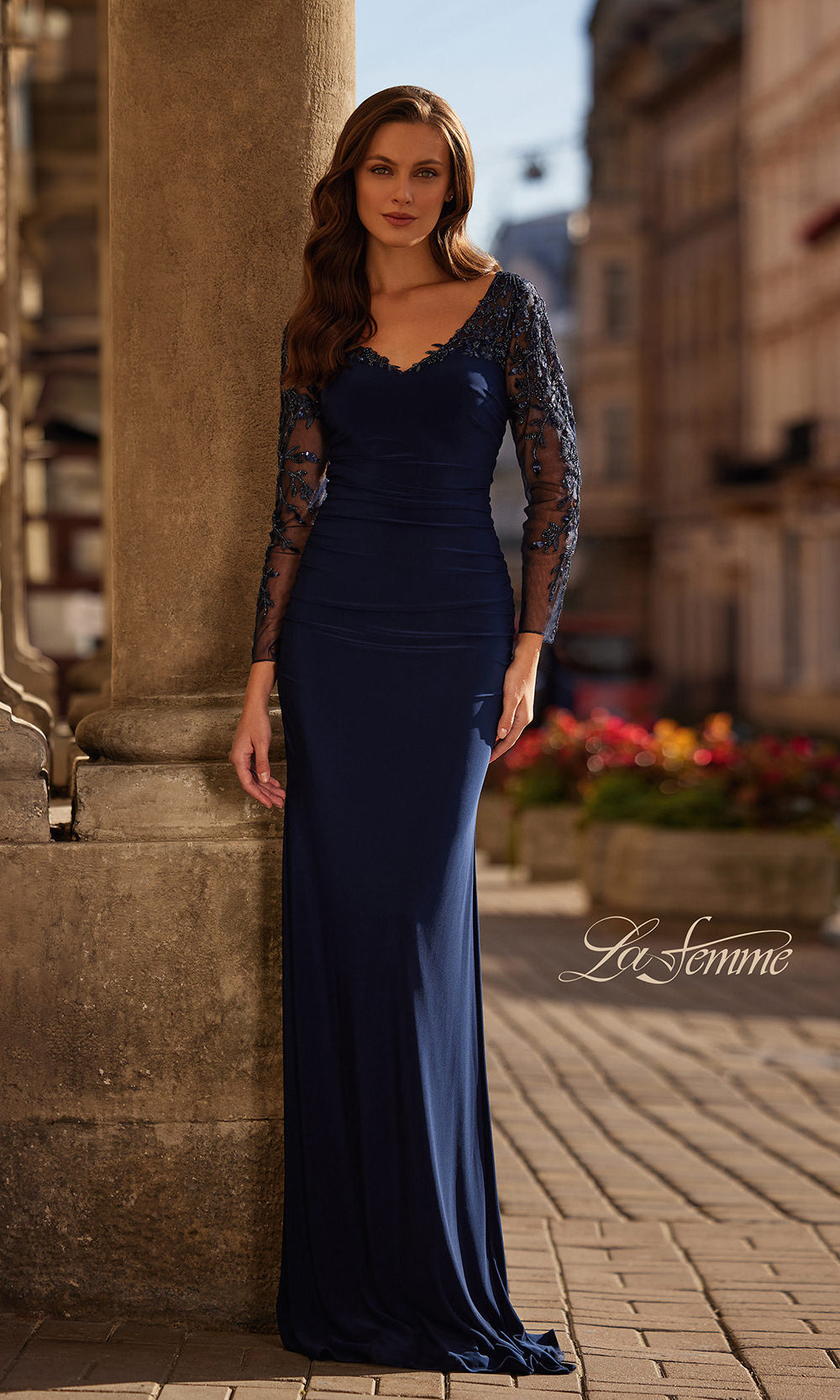 Woman in a long blue evening gown standing on a street with blurred background