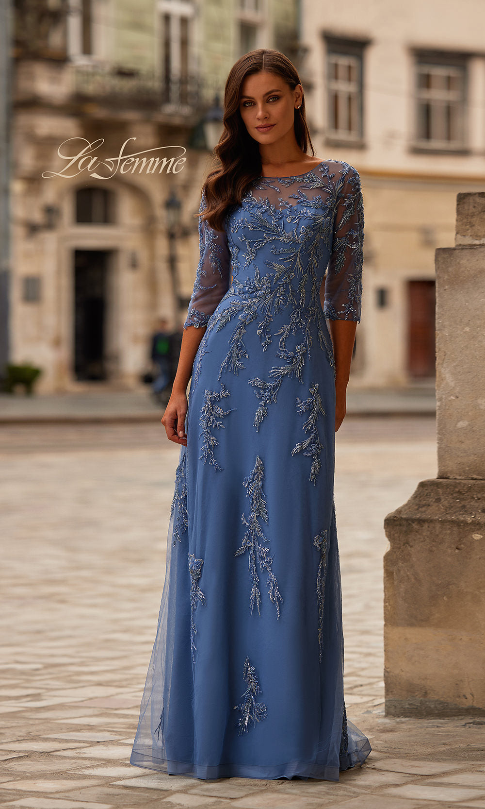 Woman wearing a blue evening gown with lace details in an outdoor setting.
