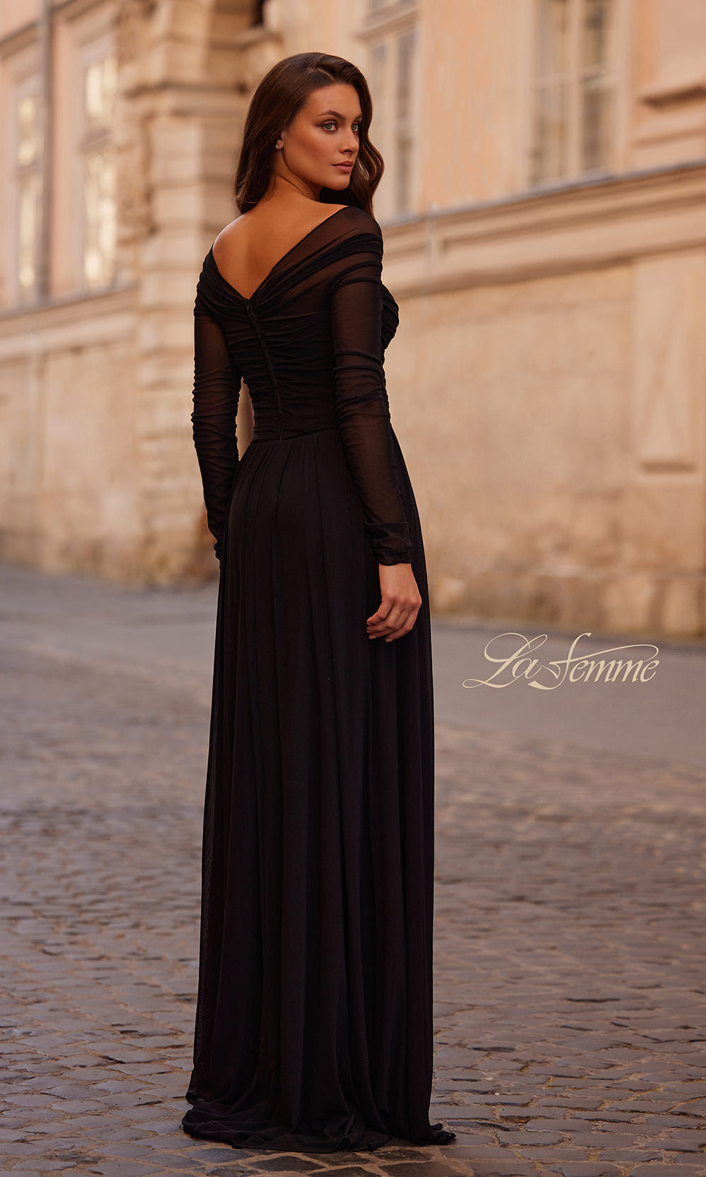 Woman wearing a black evening gown with sheer sleeves in an urban setting.