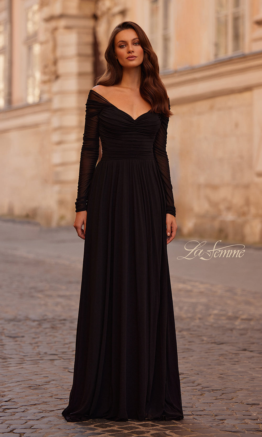 Woman wearing a black evening gown standing on a cobblestone street with a building in the background.