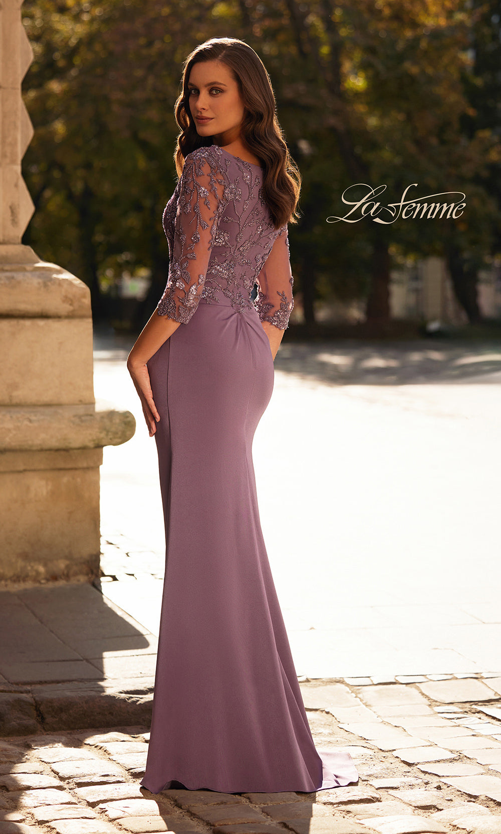 Woman wearing a purple evening gown with lace sleeves in an outdoor setting.