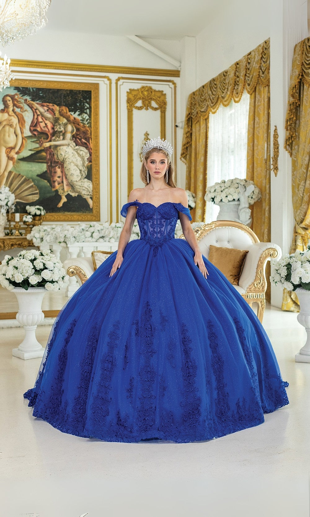 Woman in a blue evening gown standing in an elegant room with decorative walls and furniture.