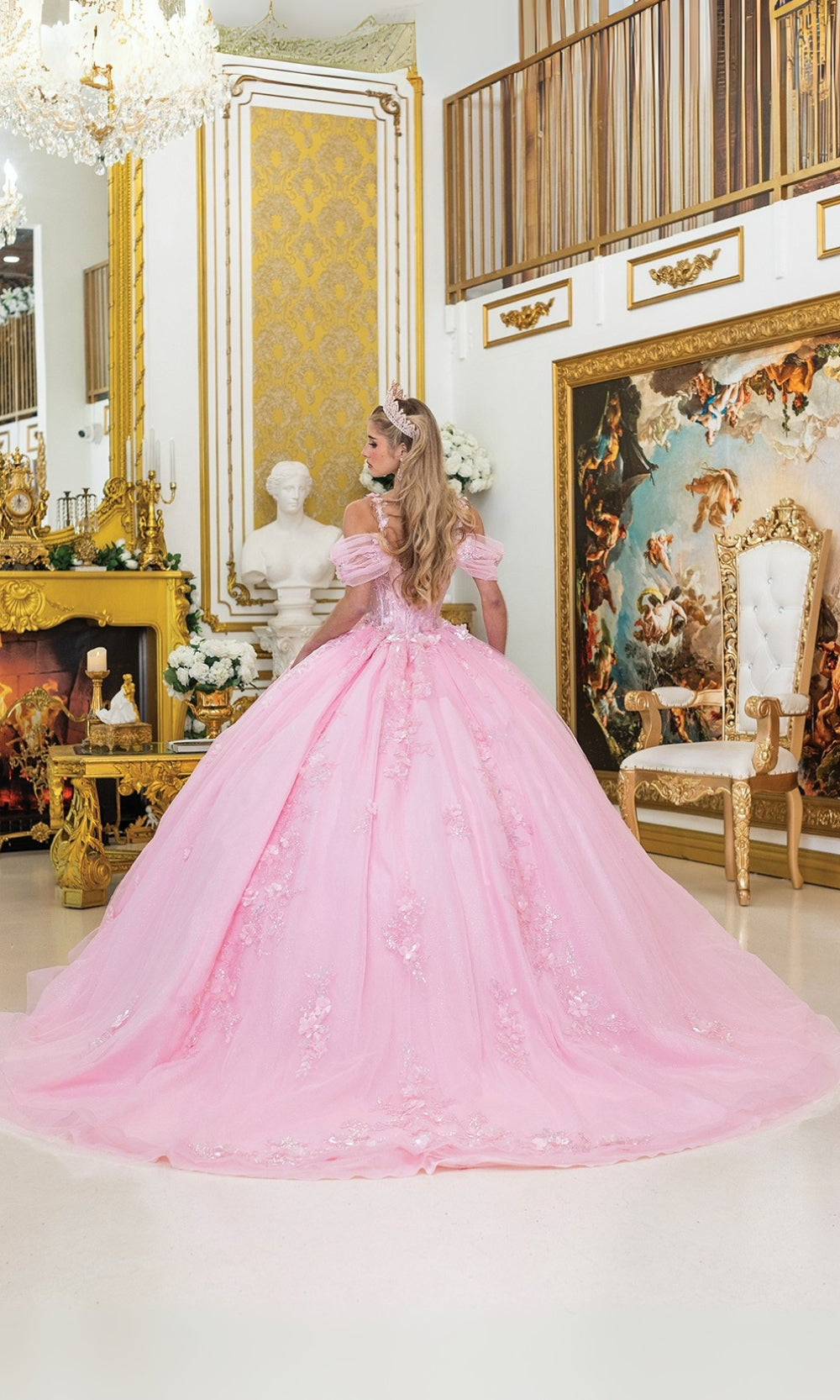 Woman in a pink gown standing in an ornate room with gold decor and artwork.