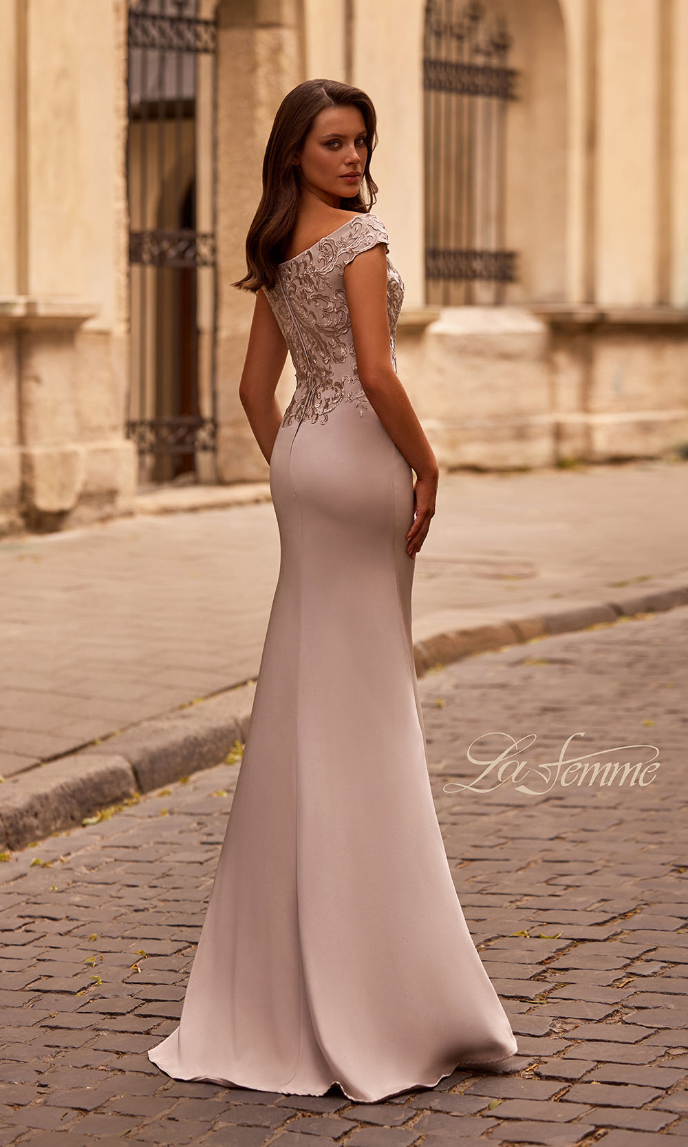 Woman in a elegant dress standing on a cobblestone street with classical architecture.