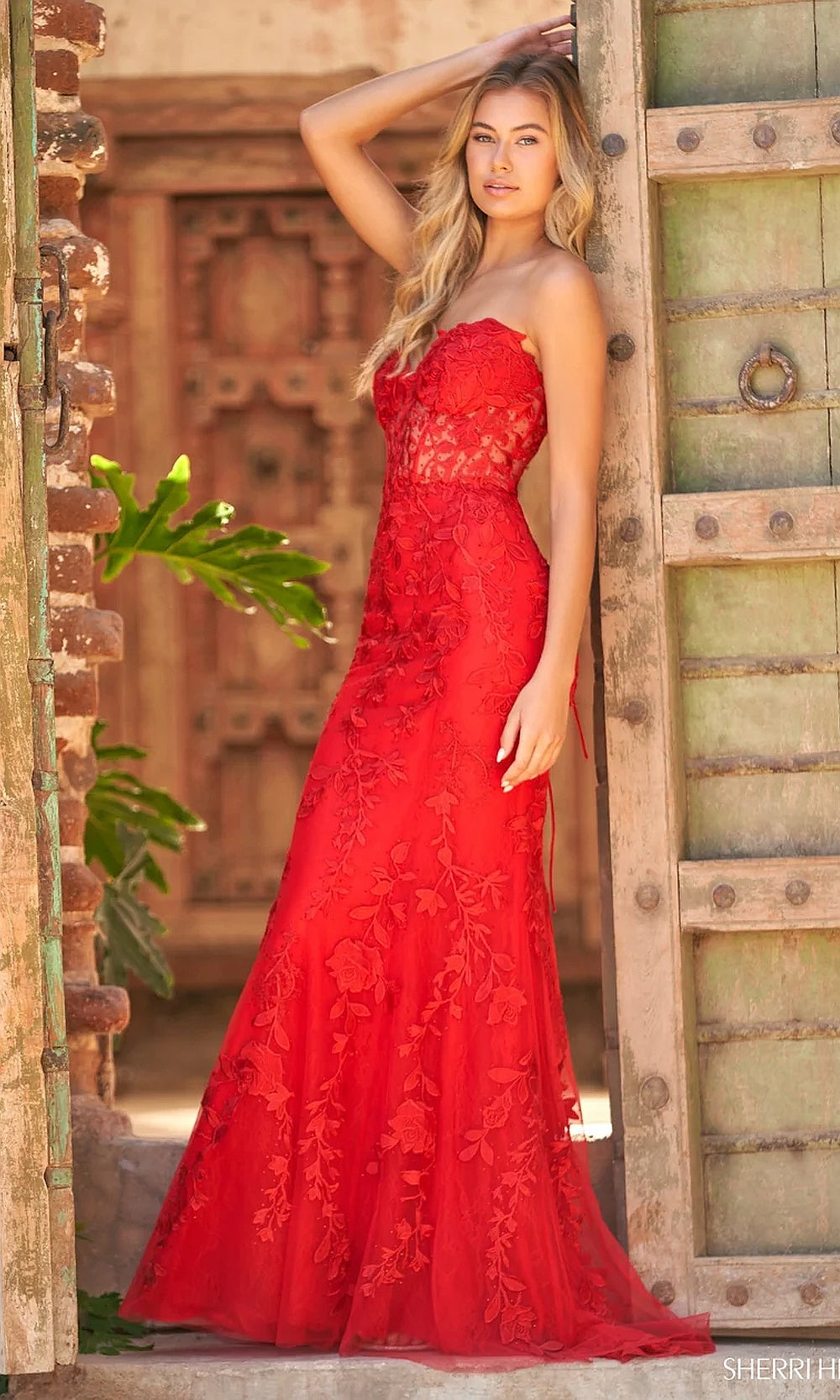 Sherri Hill 54227 Red side view prom gown with mermaid silhouette flaring below the knee, sweep train, floral lace appliqués, pageant gown styling