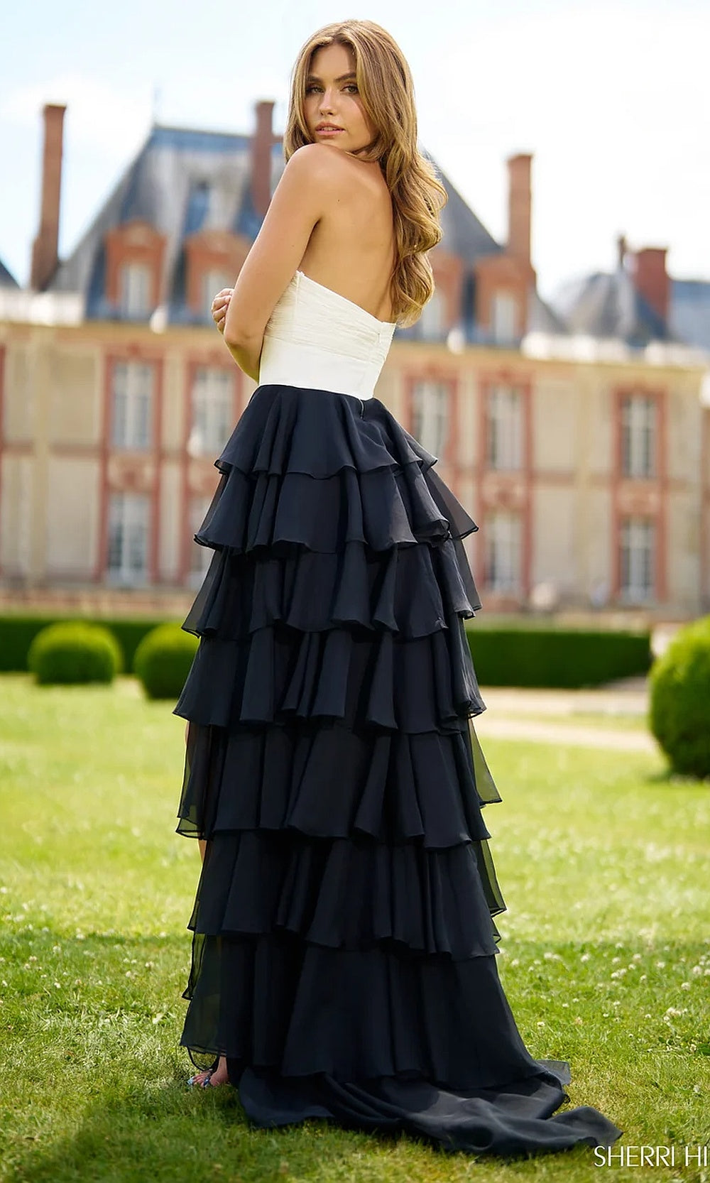 Sherri Hill 56870 Ivory Black prom gown back view showing fully open back, sweep train, tiered chiffon ruffle skirt, strapless silhouette, evening gown