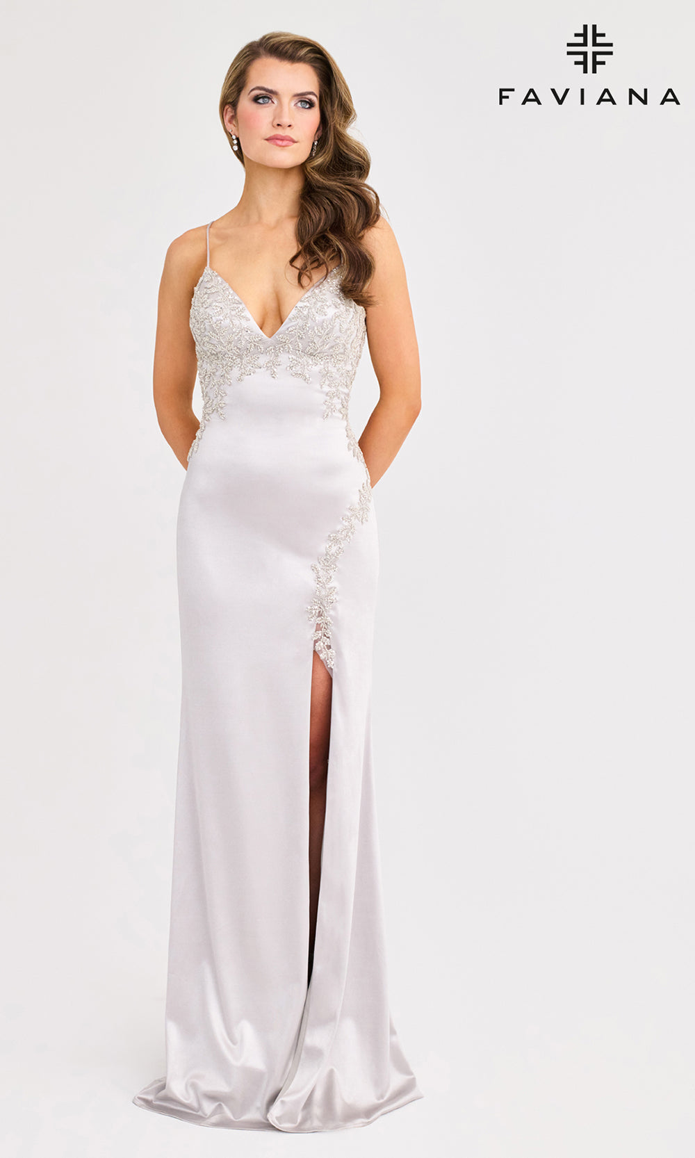 Woman wearing a white evening gown with a side slit on a white background, branded 'Faviana'.