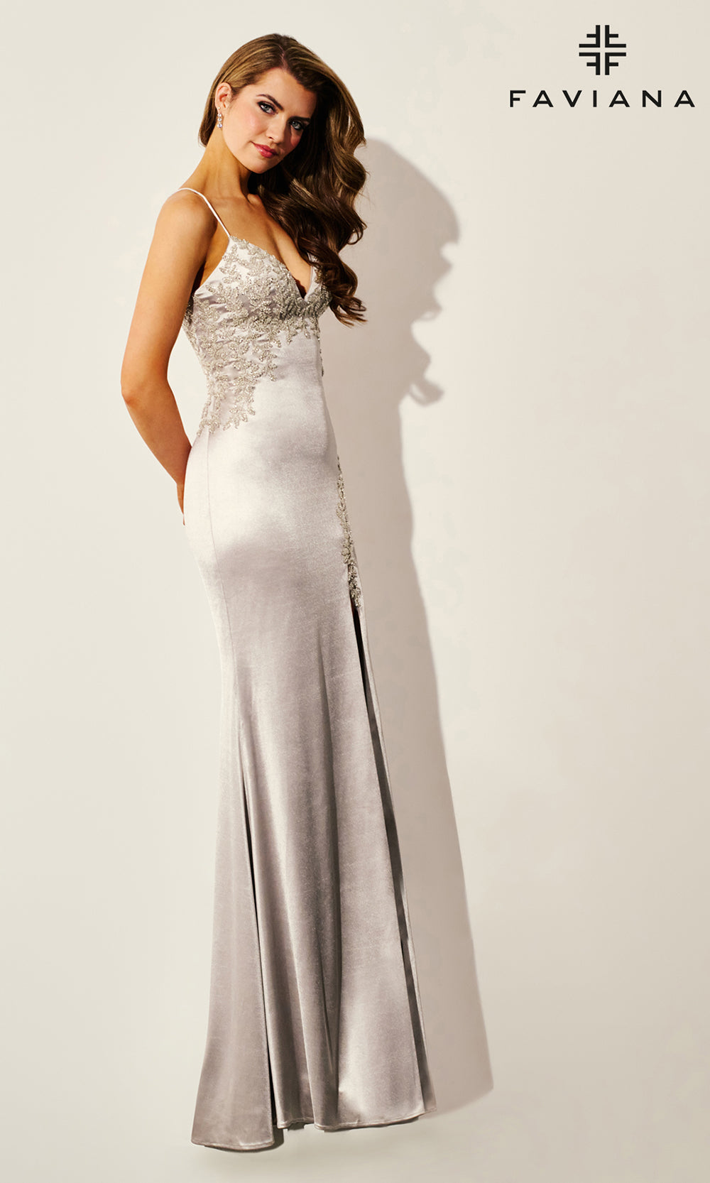 Woman wearing a silver evening gown with 'Faviana' branding on a white background