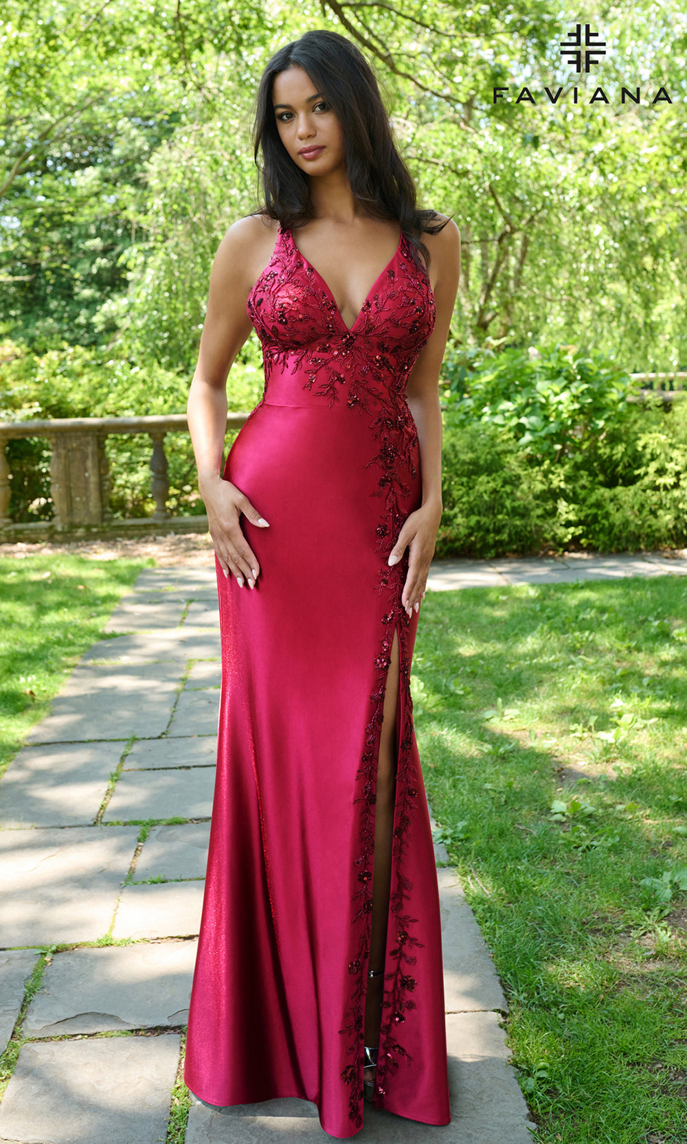 Woman in a red evening gown with floral lace details standing outdoors.