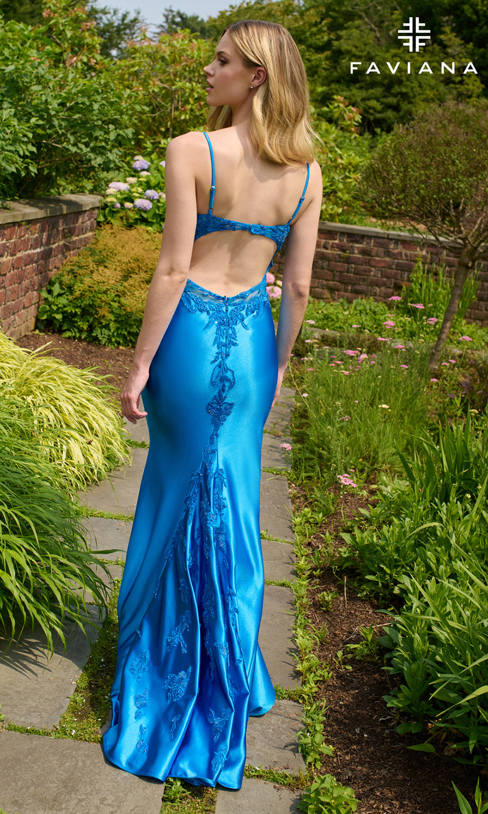 Woman in a blue evening gown walking through a garden with 'Faviana' branding.