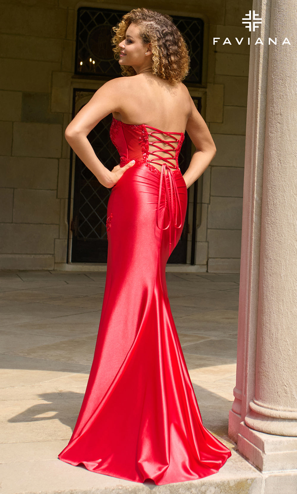 Woman wearing a red evening gown with 'Faviana' branding in an outdoor setting.
