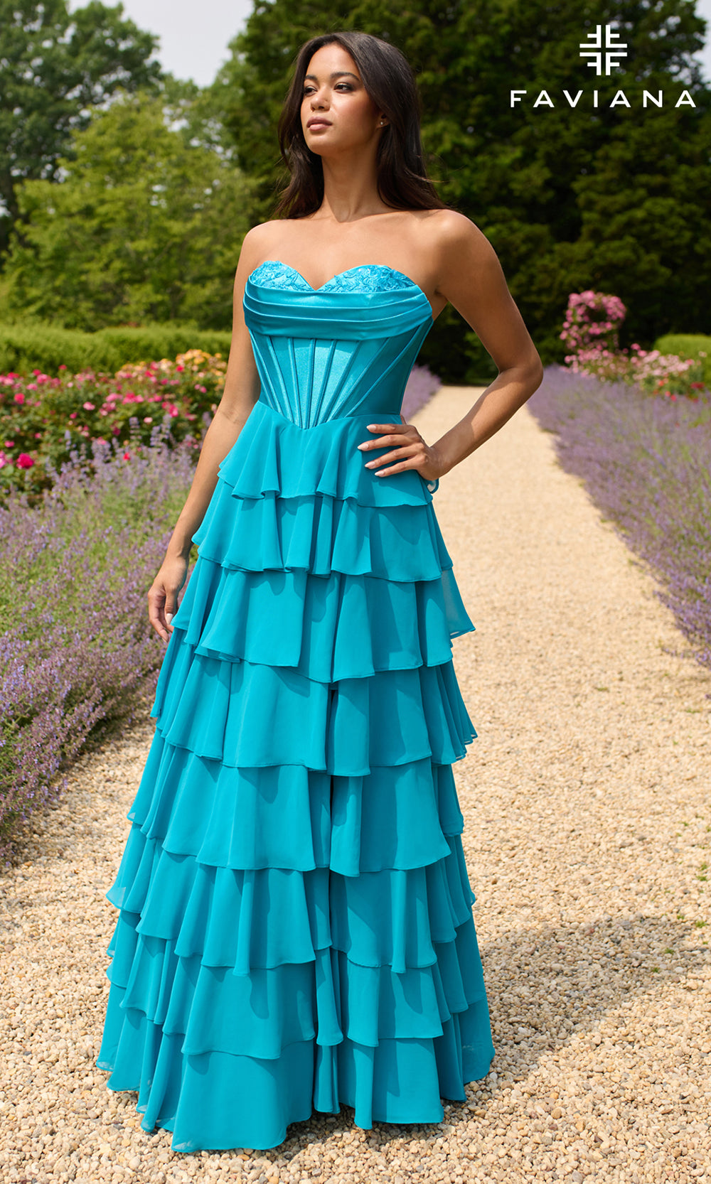 Woman in a blue strapless gown standing in a garden with 'Faviana' branding.