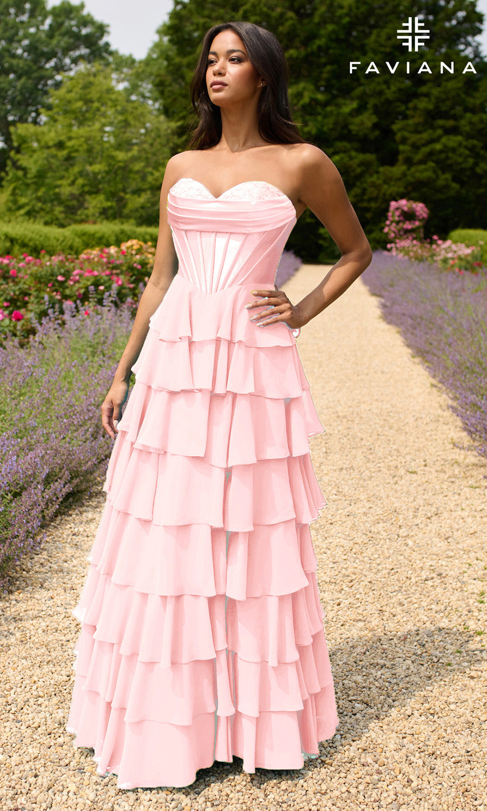 Woman in a pink strapless gown standing in a garden with 'Faviana' branding.