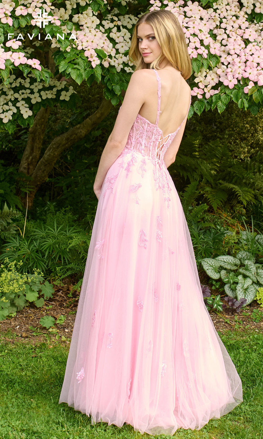 Woman in a pink dress standing outdoors with greenery and flowers in the background