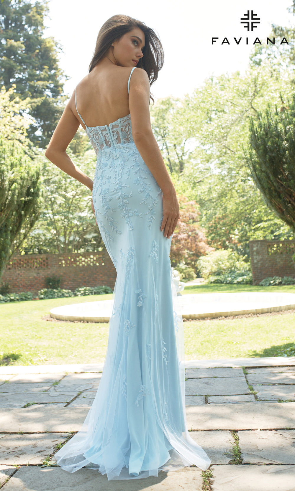Woman in a light blue evening gown with floral embellishments, standing outdoors.