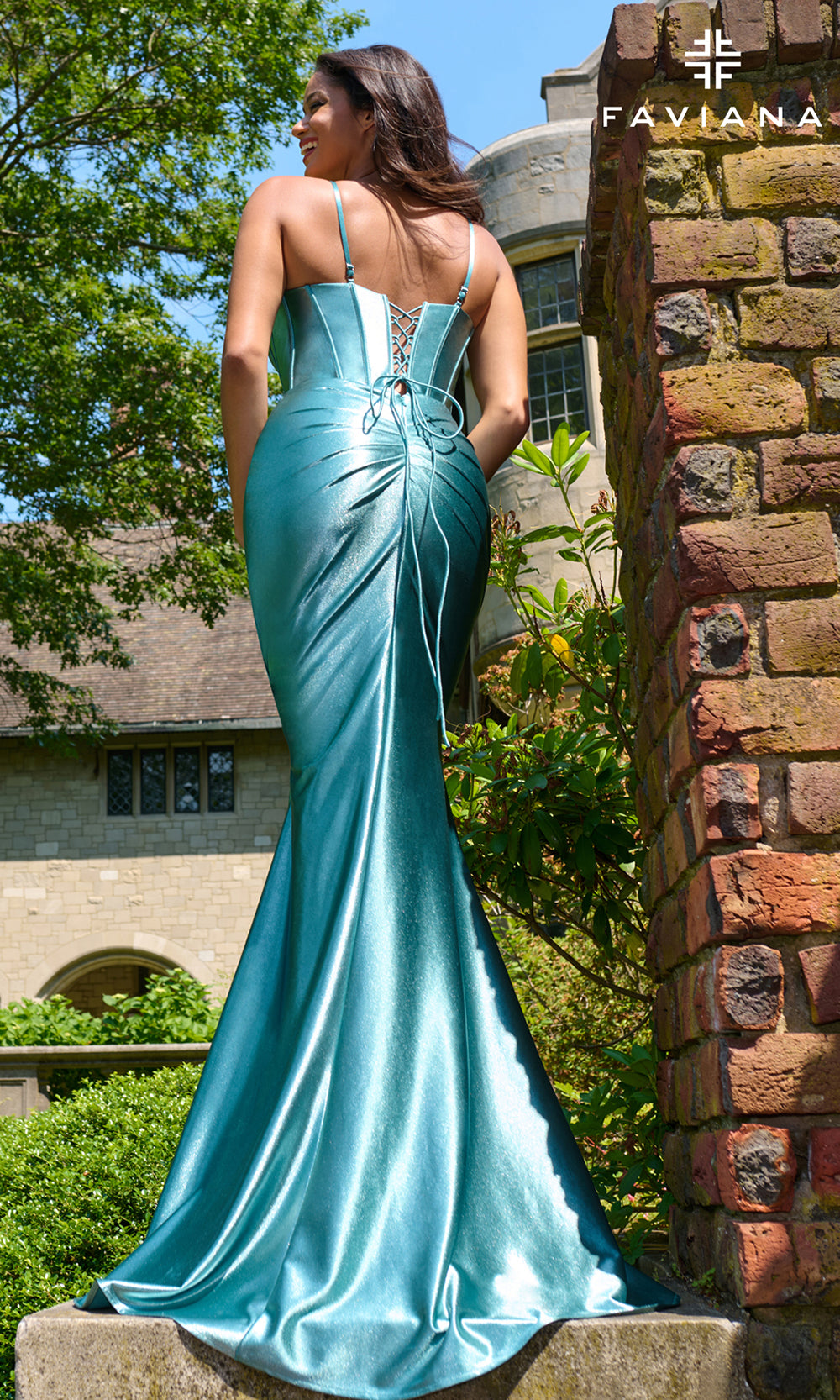 Woman in a blue evening gown standing outdoors with a building and trees in the background, featuring the brand 'Faylana'.