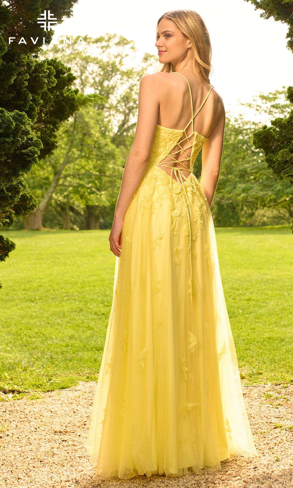 Woman in a yellow dress with lace-up back standing in a park.