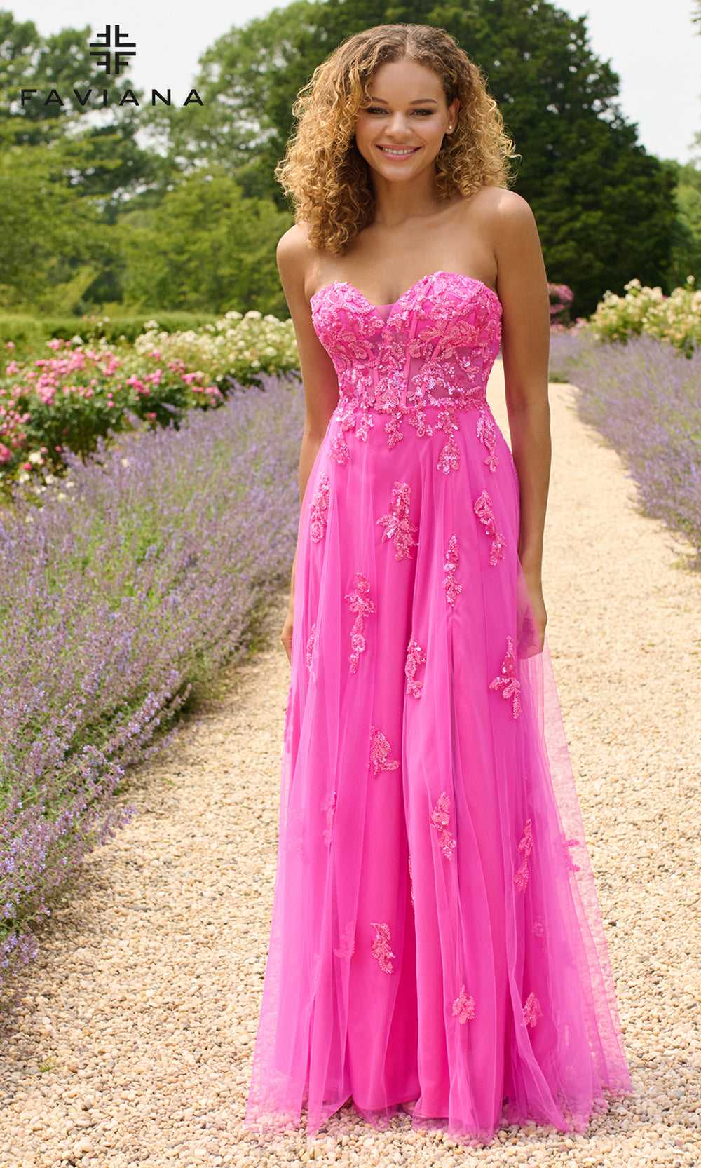 Woman in a pink dress standing in a garden with flowers and trees.