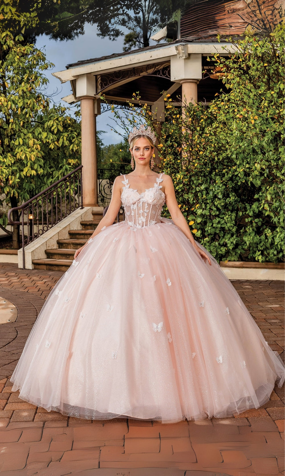 Woman in a pink wedding dress standing outdoors with greenery and a building in the background